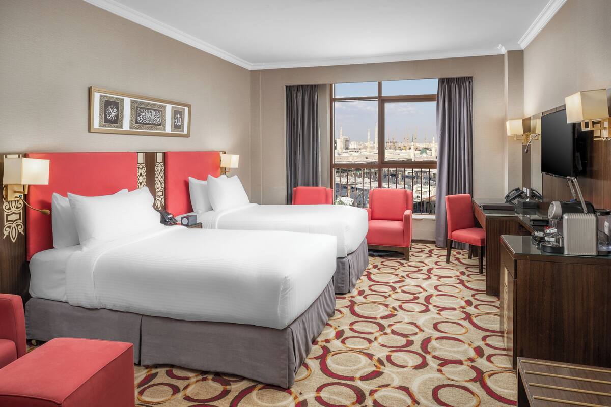 Une chambre d’hôtel avec deux lits, un bureau, une chaise et une vue sur le paysage urbain.
