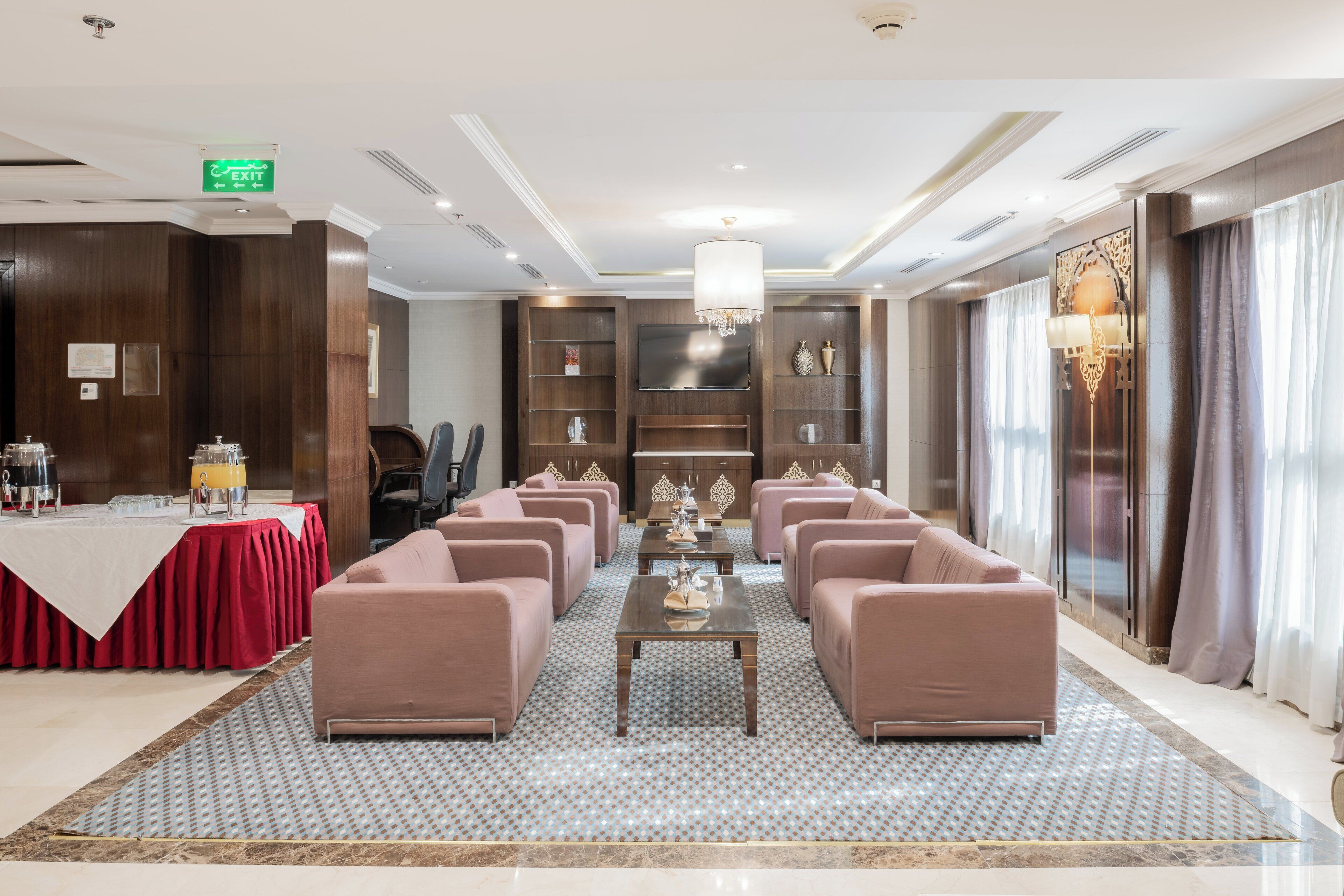 Um hall de hotel com balcão de recepção, área de estar e uma grande tela de televisão.