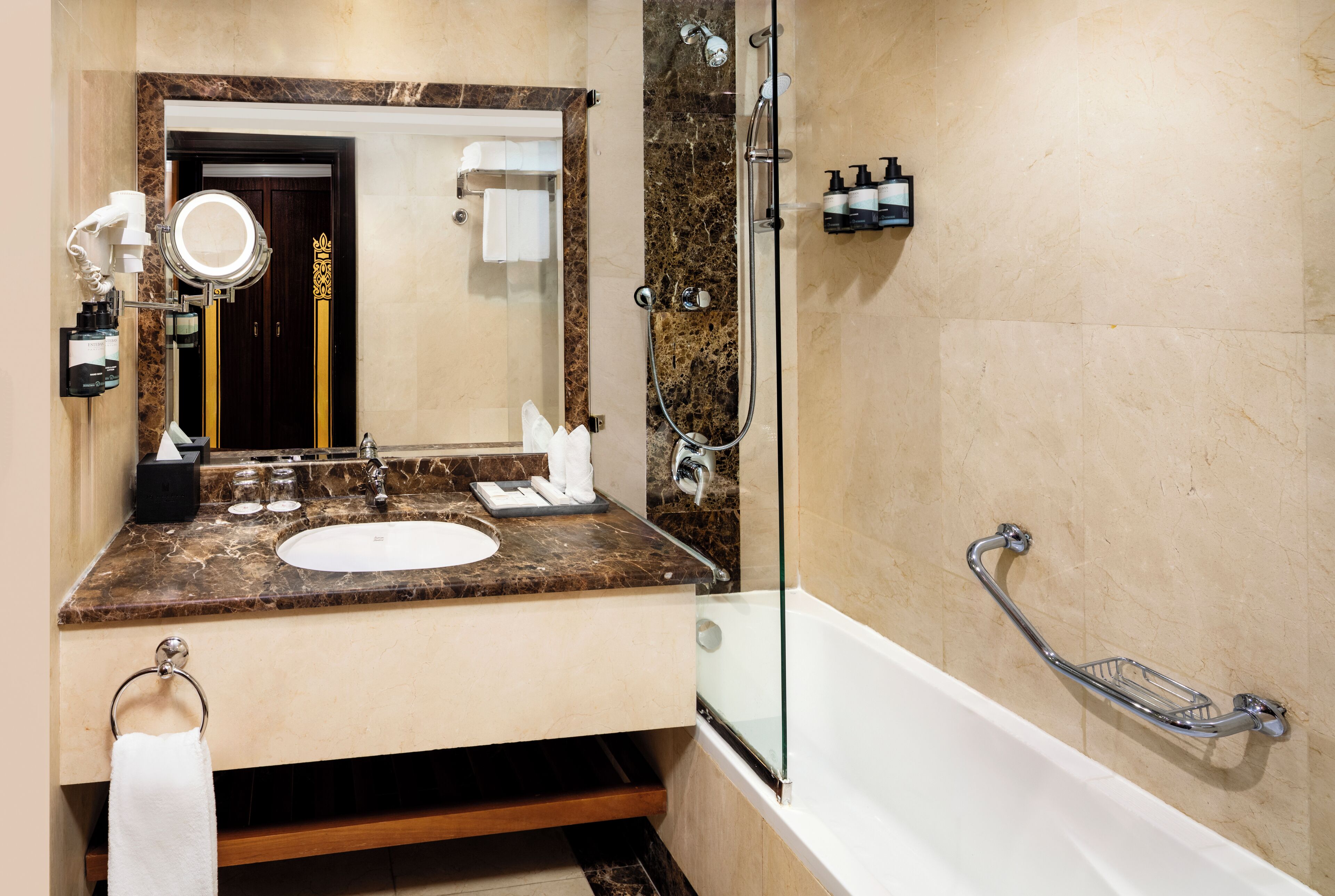 Un baño con encimera de mármol, un lavabo, un espejo grande, una ducha con puerta de cristal y una barra de apoyo.