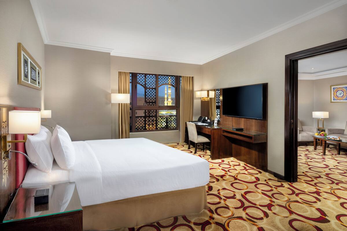 Une chambre d’hôtel avec un lit, un bureau, une télévision et une vue sur un immeuble par la fenêtre.