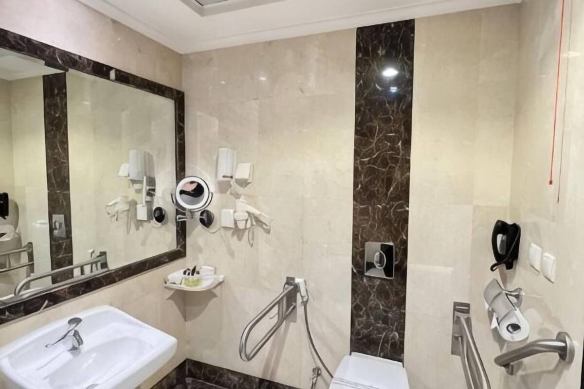 Une salle de bain moderne avec un grand miroir, un lavabo, un porte-serviettes chauffant et une douche équipée d’un pommeau de douche à main.
