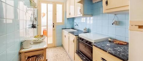 Une cuisine avec des carreaux bleu clair, un tabouret en bois, un évier et des placards.