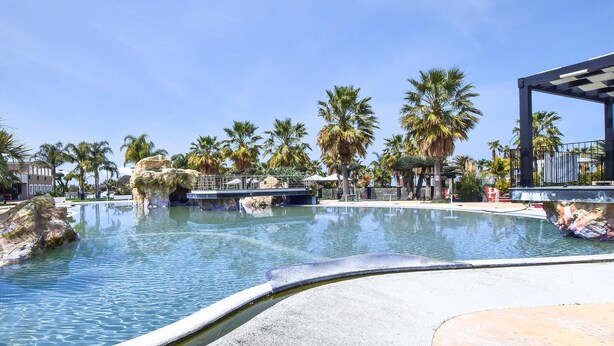 A swimming pool with a rocky edge, palm trees, and a covered area with a railing. - Lovely apartment in Palmi (Palmi)