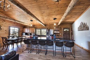 A rustic kitchen with wooden beams, a central island with bar stools, and a dining area with a leather couch.