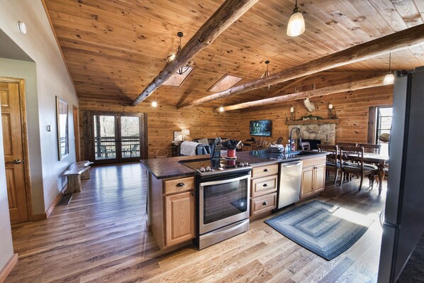 A spacious kitchen with wooden beams, a large island, and a stone fireplace.