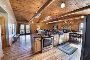 A spacious kitchen with wooden cabinets, a large island, and a stone fireplace.