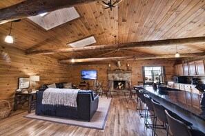 A cozy cabin interior with a fireplace, wooden walls, a television, and a bar area.