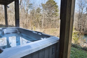 Un bain à remous doté d’une structure extérieure en bois, entouré d’un paysage naturel avec des arbres et une étendue d’eau.