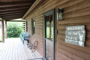 A wooden cabin with a porch, a welcome sign, and a deer silhouette.