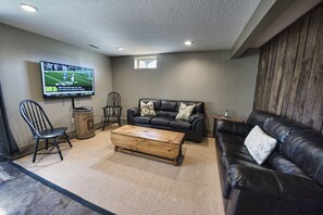A living room with a leather couch, a wooden coffee table, a television mounted on the wall, and a window.