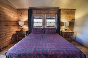 A wooden-paneled room with a large bed, two bedside tables with lamps, and a window with curtains.