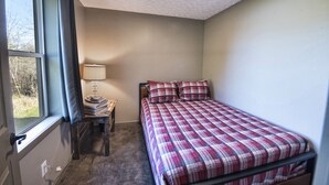Ein Schlafzimmer mit einem Bett, einem Nachttisch, einer Lampe und einem Fenster.