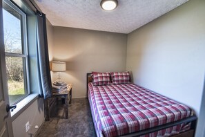 A bedroom with a bed, a nightstand, a lamp, and a window.