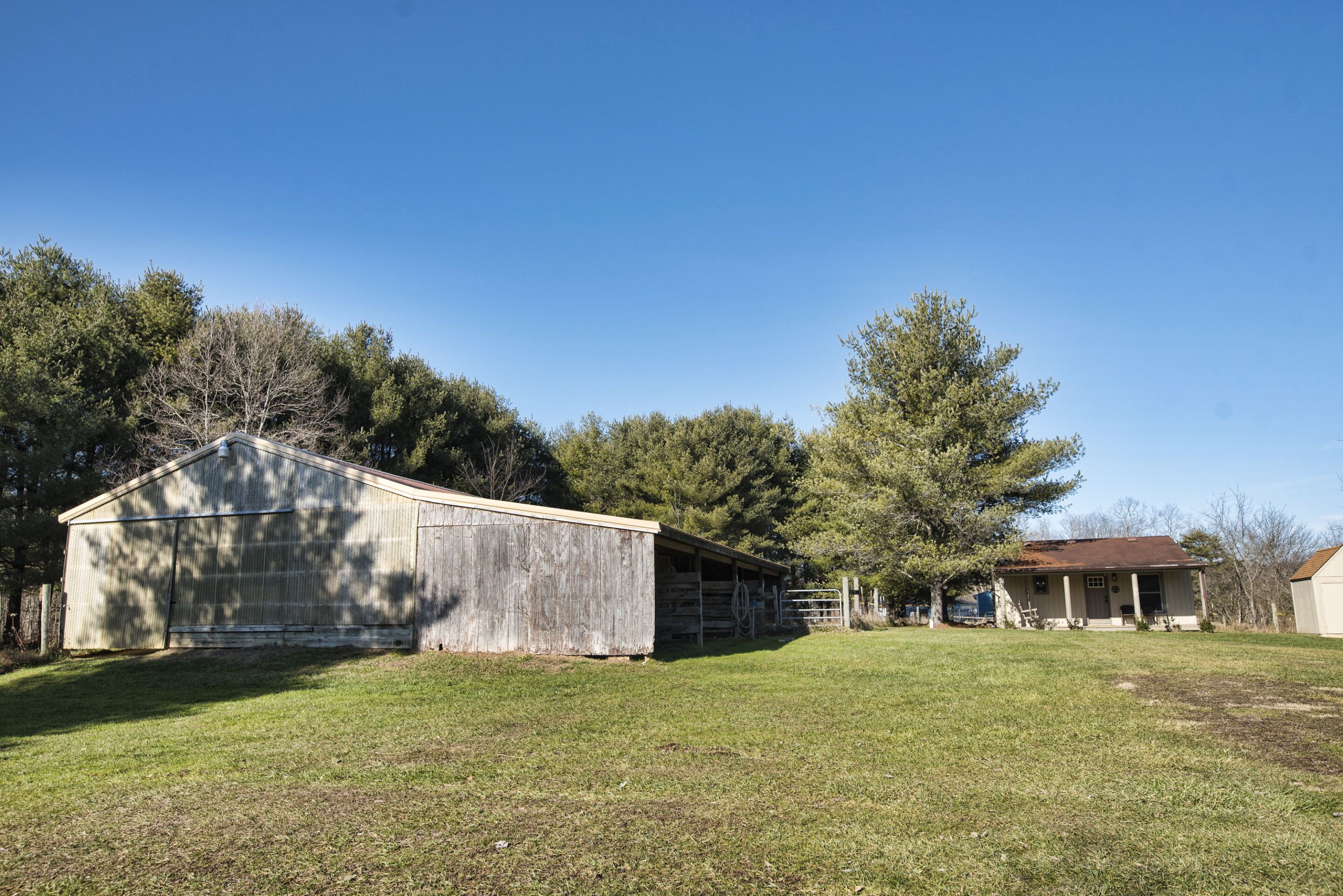 Une propriété rurale comprenant une grande grange, une petite maison et un champ d’herbe.