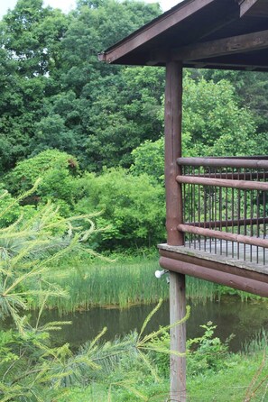 A wooden deck with a railing overlooking a pond surrounded by lush greenery.
