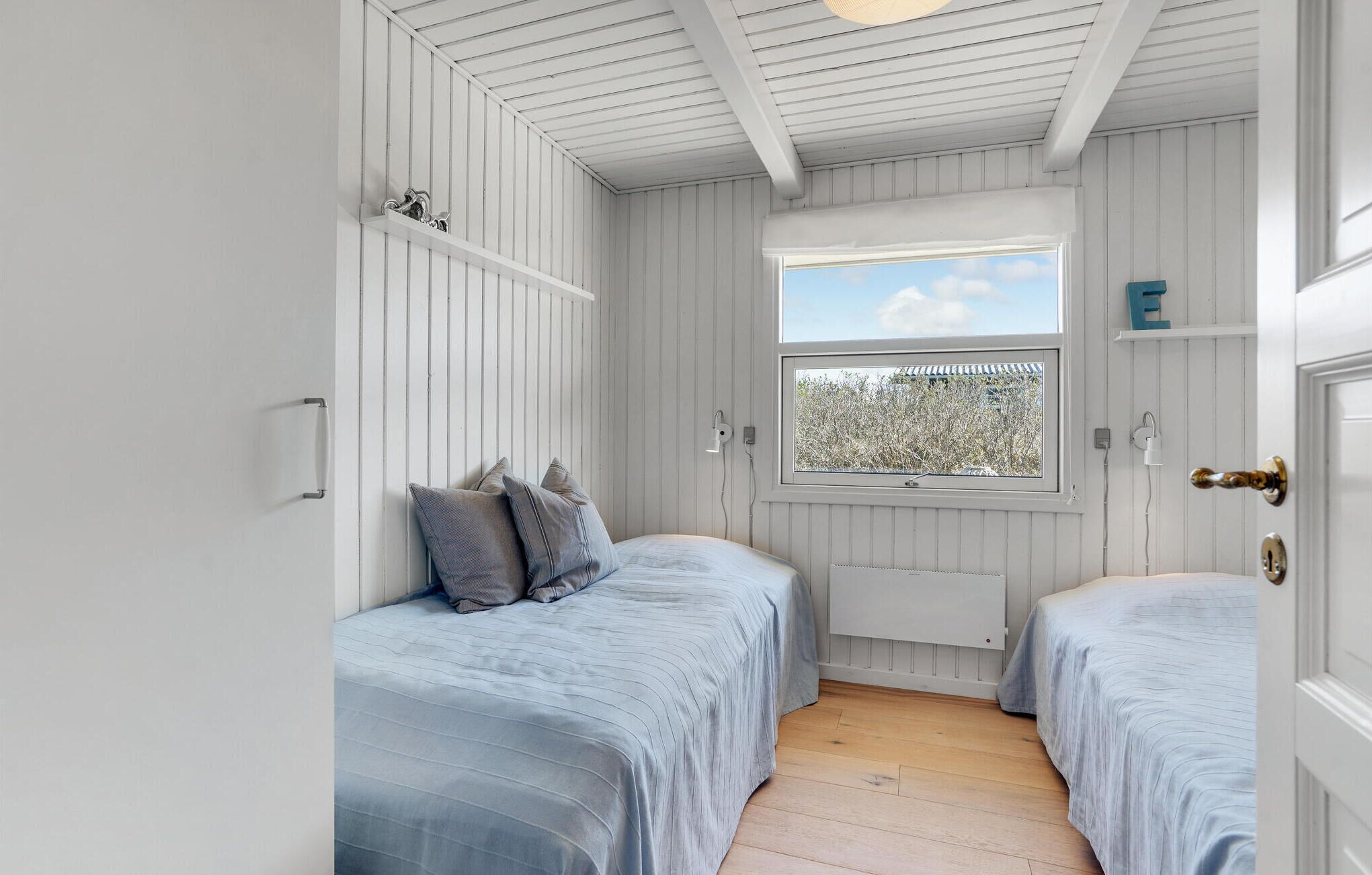 Ein Schlafzimmer mit zwei Betten, einem Fenster mit Ausblick und weißen Holzwänden.