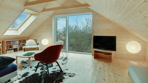 Ein geräumiges Dachzimmer mit Holzbalken, einem großen Fernseher und einer gemütlichen Sitzecke mit einem roten Sessel und einem weißen Sofa.