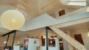 Ein geräumiger Innenraum mit hohen Decken, Holzbalken, einer Treppe und einer Küchenzeile.