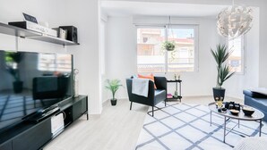 Sala de estar moderna com televisão de tela plana, sofá, mesa de centro e uma grande janela com vista para edifícios.