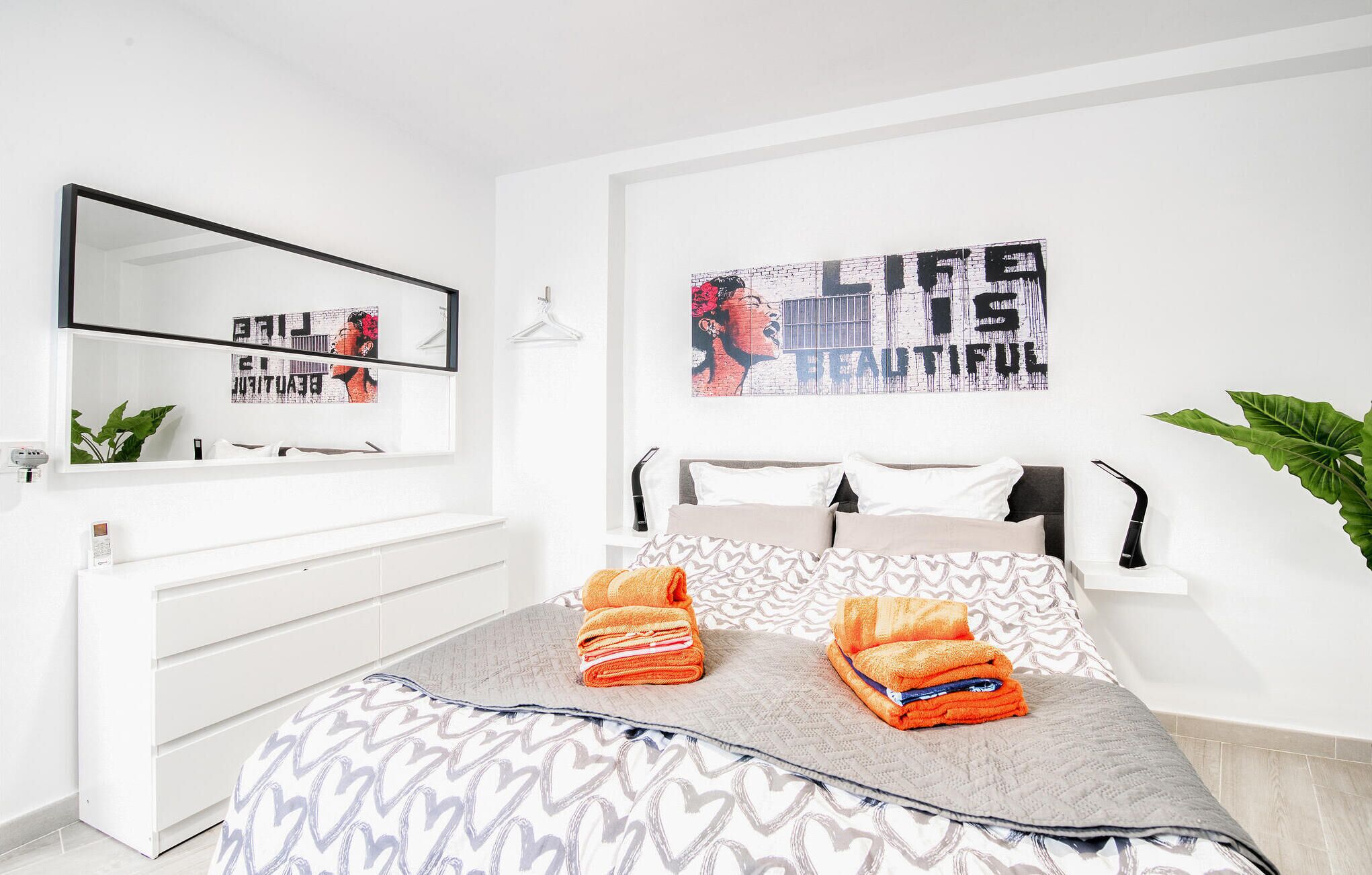 Ein modernes Schlafzimmer mit Bett, Nachttisch, Spiegel und einem Wandbild.