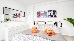 Um quarto moderno com uma cama, mesa de cabeceira, espelho e uma obra de arte na parede.