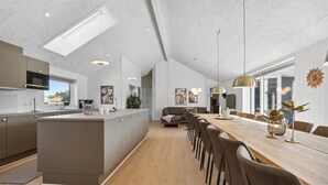 A modern kitchen with a central island, a dining area with a long wooden table and chairs, and a living space with a sofa and a TV. - Pet friendly home in Rømø with sauna (Rømø)