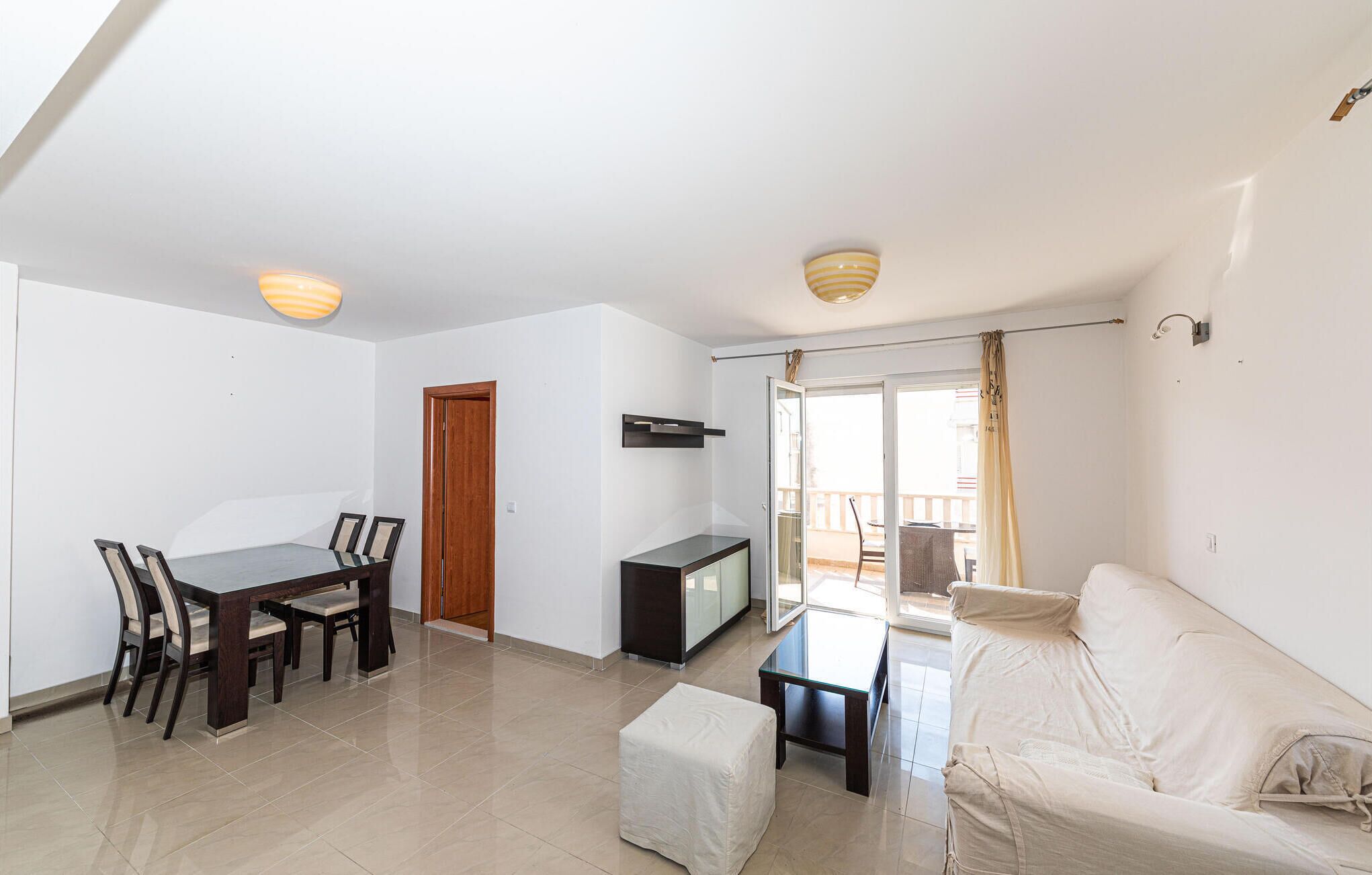 Sala de estar com mesa de jantar, cadeiras, sofá, televisão e varanda com vista.
