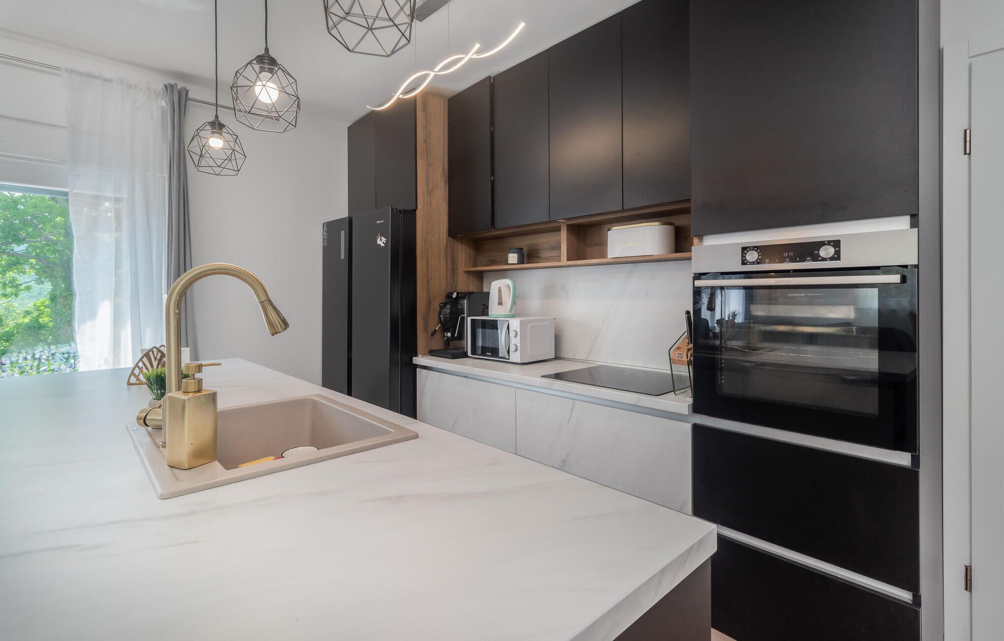 A modern kitchen with a white countertop, a gold faucet, a built-in oven, and a coffee machine.