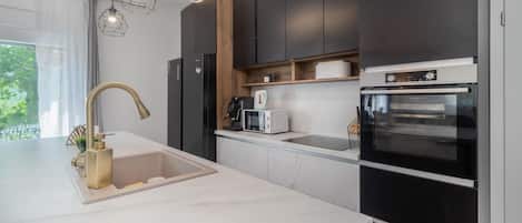 A modern kitchen with a white countertop, a gold faucet, a built-in oven, and a coffee machine.