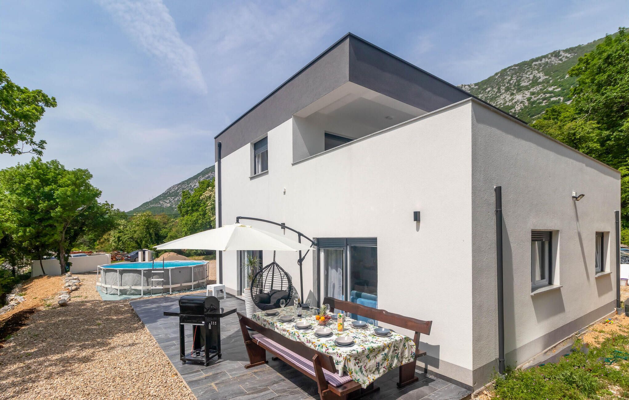Een modern huis met twee verdiepingen, een terras, een barbecue en een zwembad.