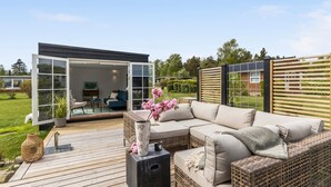 Ein Außenbereich mit einer modernen Glasdoor, einem Korbsesselsofa und einem Holzterrasse.