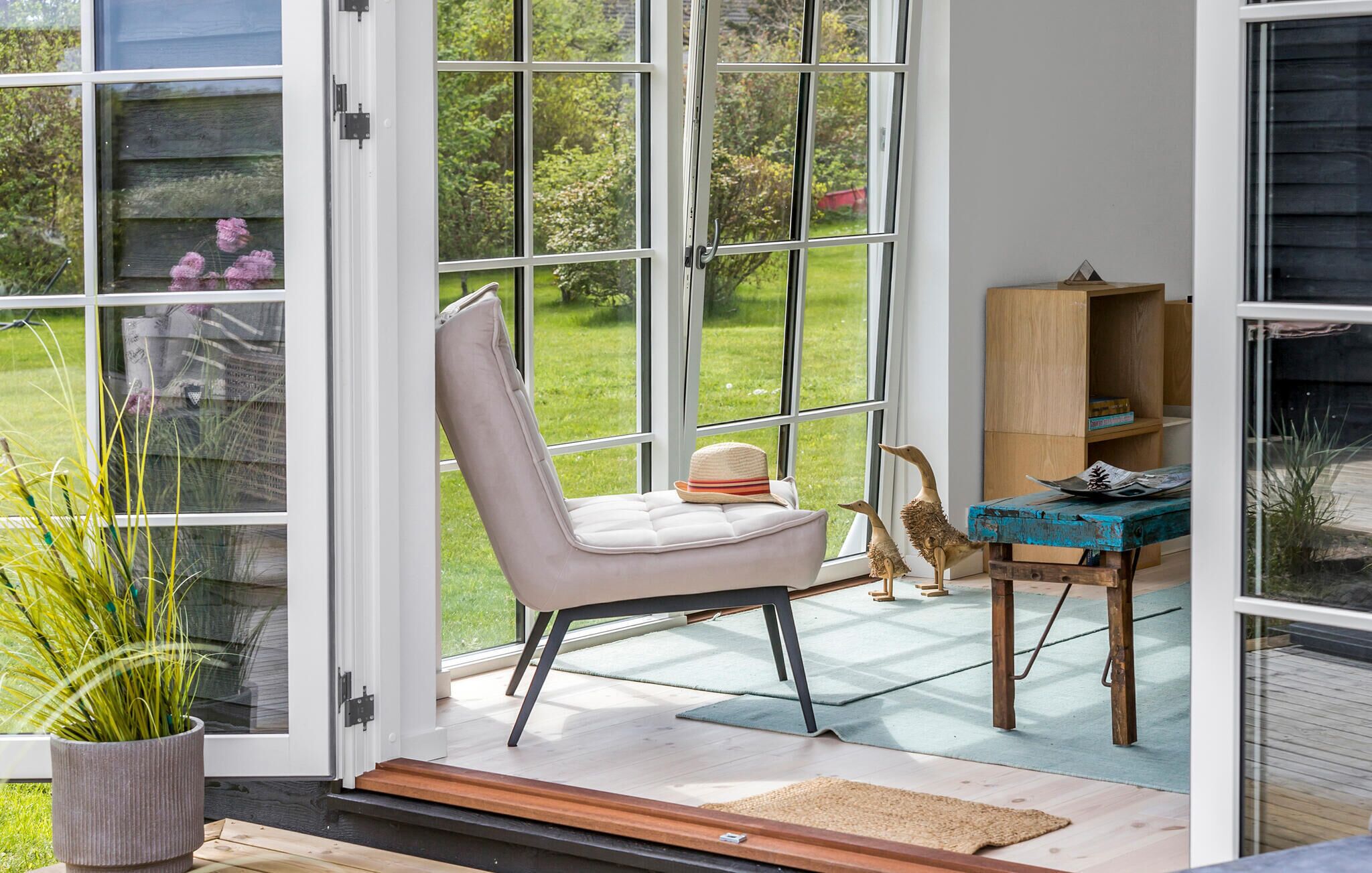 Ein modernes Interieur mit einer großen Glasdoor, einem gepolsterten Sessel, einem Holztisch und einem rustikalen Bücherregal.