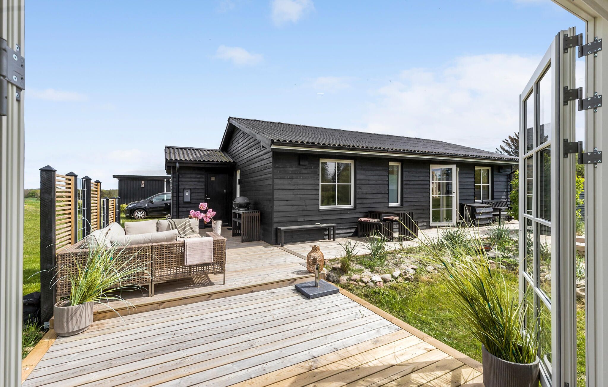 Ett modernt trähus med en veranda, utomhusmöbler och en grillplats.
