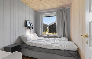 Een slaapkamer met een bed, een raam, een wandplank met foto’s en een deur met een sleutelgat.