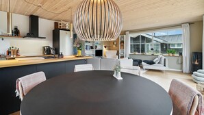 Eine moderne Küche mit Kochinsel, ein Essbereich mit rundem Tisch und ein Wohnbereich mit Sofa und Kamin.
