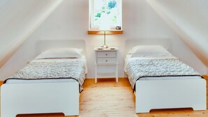 Ein kleiner, gut beleuchteter Raum mit zwei Einzelbetten, einem Nachttisch mit Lampe und einem Fenster, das für natürliches Licht sorgt.