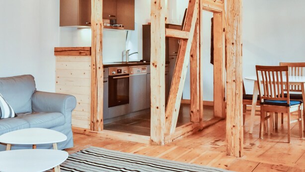 Ein modernes Interieur mit Holzboden, einem grauen Sofa, einem Esstisch und einer Küchenzeile.