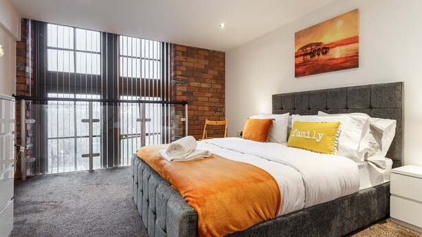 A modern bedroom with a large bed, a brick wall, and a cityscape view.