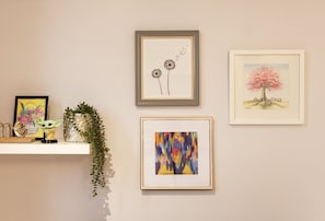 Un mur orné de quatre œuvres d’art encadrées, une étagère avec des objets décoratifs et une plante suspendue.