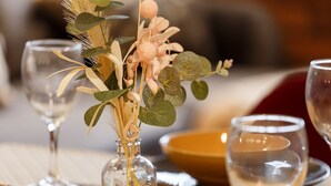 A table setting with a glass vase containing decorative foliage and a candle.
