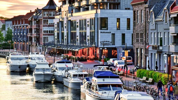 Una zona ribereña con barcos amarrados a lo largo del canal, edificios con comercios y un paseo peatonal.