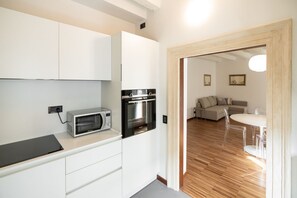 Eine kompakte Küche mit modernen Geräten, ein Essbereich mit weißem Tisch und Stühlen sowie ein Wohnzimmer mit Sofa und Couchtisch.