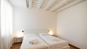 Ein Zimmer mit zwei Einzelbetten, Holzboden, weißen Wänden und einer geneigten Decke.