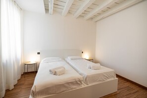 Ein Zimmer mit zwei Einzelbetten, Holzboden, weißen Wänden und einer geneigten Decke.