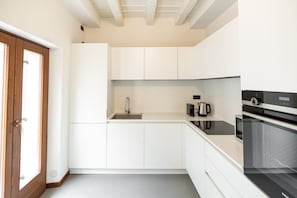 Una cocina moderna con muebles blancos, un lavamanos de acero inoxidable, una cafetera y un horno empotrado.