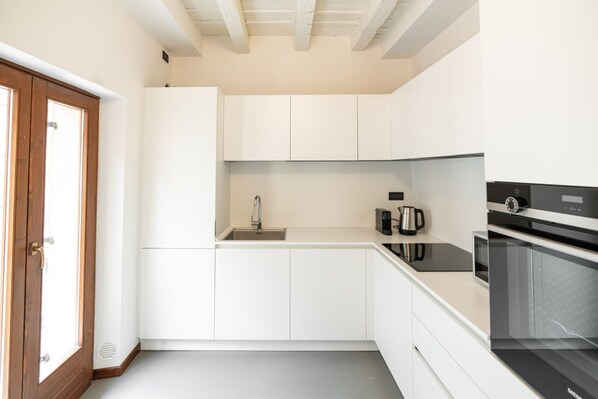 A modern kitchen with white cabinetry, a stainless steel sink, a coffee maker, and a built-in oven.