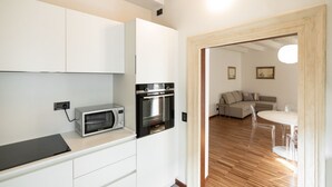 Eine kompakte Küche mit modernen Geräten, ein Essbereich mit weißem Tisch und Stühlen sowie ein Wohnzimmer mit Sofa und Couchtisch.