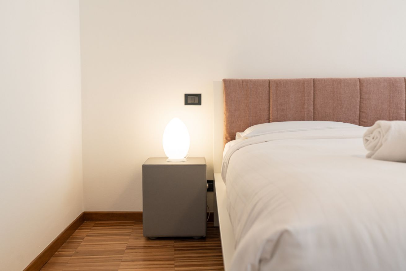 A neatly made bed with a headboard, a bedside lamp, and a wooden floor.