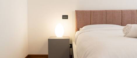 A neatly made bed with a headboard, a bedside lamp, and a wooden floor.