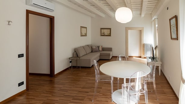 Ein geräumiges Wohnzimmer mit Holzboden, einem weißen runden Tisch mit klaren Stühlen, einem beigen Sofa und einem Deckenventilator.